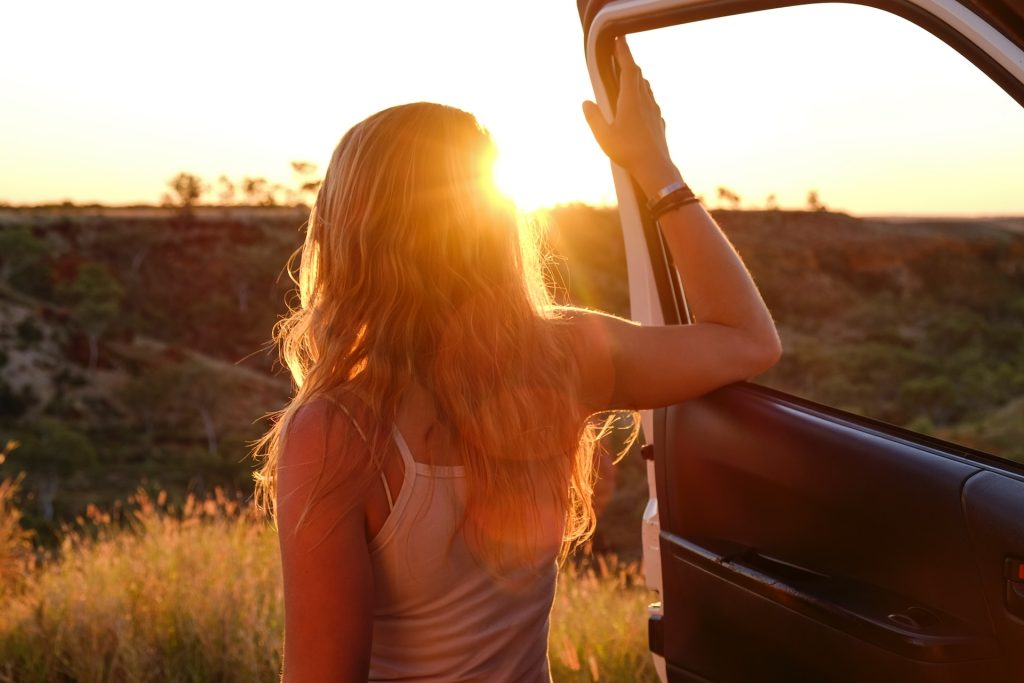 Girl holding onto a car door at sunset