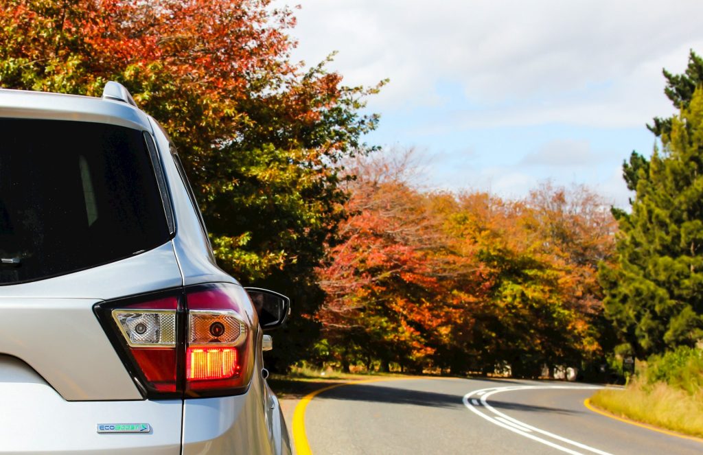 close up of silver suv driving down a road in fall